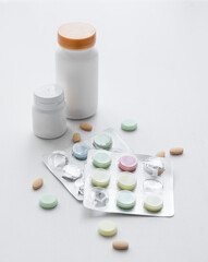 Assorted pills, vitamins and nutritional supplements in different colors with white bottles on a white background.