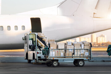 Close-up detail view of cargo cart trolley full with commercial parcels against turboprop cargo plane. Air mail shipping and logistics. Import export operations. Commercial charter flight service