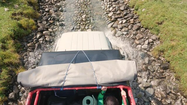 SUV driving along a river and rocks in the mountains. Top view of the bonnet, people in the cabin and the road. Off-road trip on a mountain road