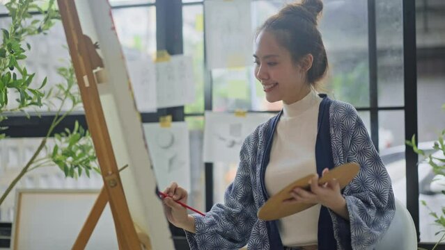 Innovative asian female painter using red paint on big canvas,holding tube of oil paint,fine art artist drawing,Abstract acrylic painting in the art studio.asian woman painting brush on canvas
