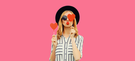 Portrait of beautiful young woman blowing her lips sends kiss with sweet red heart shaped lollipop