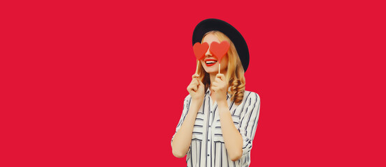 Portrait of happy cheerful young woman with sweet red heart shaped lollipop on stick on pink