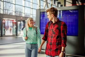 A young happy couple is holding hands at train station while walking.