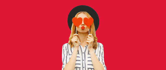Portrait of beautiful young woman blowing her lips sends kiss with sweet red heart shaped lollipop