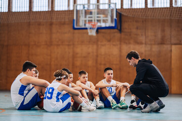 A junior basketball team is sitting on court with their coach.