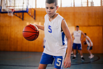 A young basketball kid in action dribbling a ball on training at court.