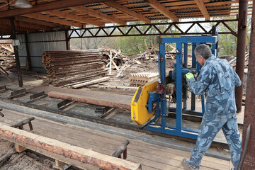 A worker saws a tree trunk on a machine. The sawmill. The process of processing logs at a sawmill. The concept of manufacturing pallets for transportation.