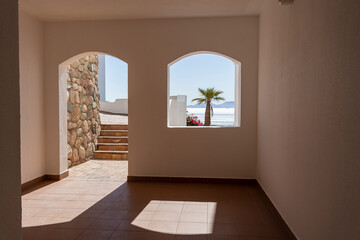 Window hole in the white stone wall of a building overlooking the Red Sea and a palm tree on a tropical beach in resort town Sharm El Sheikh, Egypt