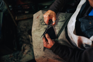 Close up of senior artisan's hands cutting leather with scissors.
