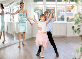 Boy and girl kids repeat movement while taking rumba dancing lessons. Female teacher conducts class...