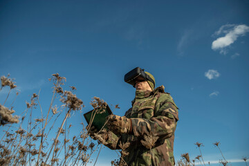 Modern technology in the army. Warfare analytic operator using vr virtual reality glasses checking coordination of the military team with tablet device augmented reality operating troops outdoors