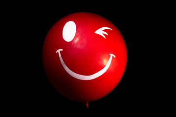 Red smiling inflatable balloon on a black background. Winking air balloon in the dark. A creepy...