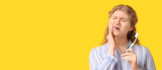 Young woman suffering from tooth ache while brushing teeth on yellow background with space for text