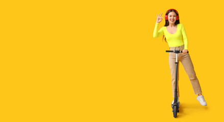 Beautiful young woman in headphones and with kick scooter showing OK gesture on yellow  with space for text © Pixel-Shot