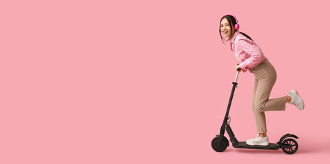 Beautiful young woman in headphones riding modern electric kick scooter on pink background with space for text