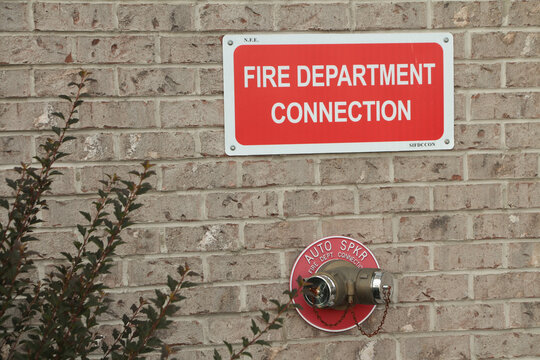 fire department connection sign on beige brick wall with two twin connections below from one spout in red circle auto spkr, white on red