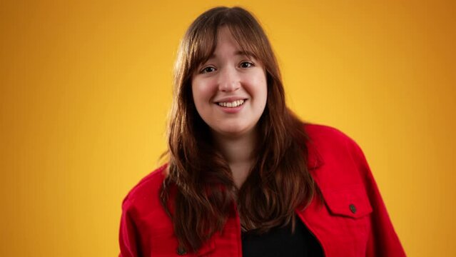 Come here, follow me. Beautiful girl long hair in red jacket making beckoning gesture with one finger, inviting to approach, looking playful flirting. Isolated on yellow background 