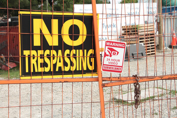 no trespassing warning 24 hour video surveillance signs on orange locked gate for dirt yard parking...