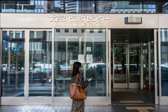 Tokyo, Japan, 2 November 2023: Woman Standing in Front of Bunkyo Civic Center Entrance.