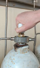 An employee's hand opens the valve of an acetylene cylinder against the background of pipes in the gas ramp