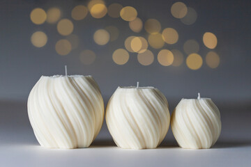 Three soy wax handmade candles of different size on white table with gray background, bokeh and...
