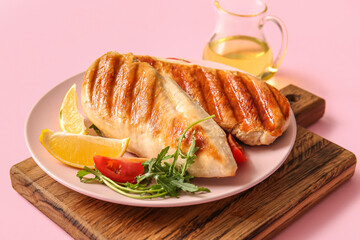 Plate of tasty grilled chicken breast with arugula, tomatoes and lemon on pink background