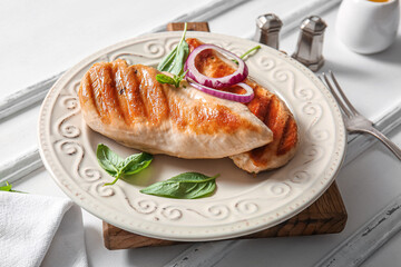 Plate of tasty grilled chicken breast with basil and red onion on white background