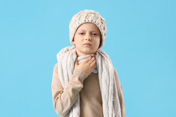 Ill little boy in hat suffering from sore throat on blue background