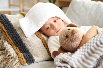 Ill little boy with towel and toy bear lying on sofa at home, closeup