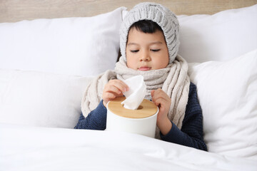 Ill little Asian boy taking tissue from box in bedroom