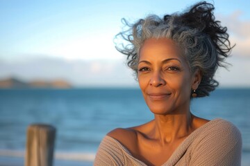 A serene lady gazes up at the clear blue sky, her grey hair and shirt blending with the tranquil surroundings of the beach as she smiles, embracing the beauty of nature