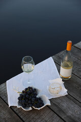 picnic by the lake with white wine, grapes, cheese. aesthetic picnic for girls. Picnic at the wooden pier by the lake.