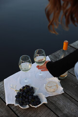 picnic by the lake with white wine, grapes, cheese. aesthetic picnic for girls. a woman takes a glass of white wine with her hand