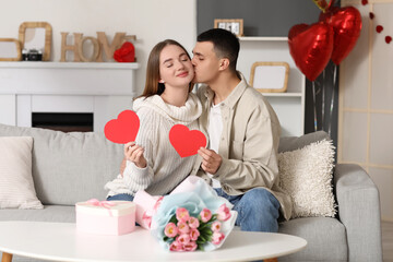 Beautiful young couple with gift box, bouquet of flowers and paper hearts celebrating Valentine's...