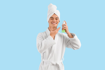 Teenage boy in bathrobe with skincare product after shower on blue background