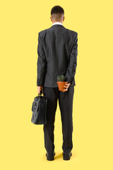 Young businessman with hemorrhoids and cactus on yellow background, back view