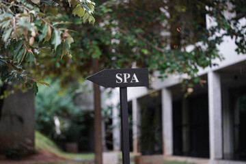 Wooden spa sign in the forrest with green leaves and white building.