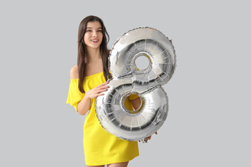 Beautiful young woman with silver air balloon in shape of figure 8 on grey background....