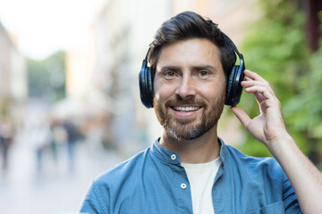 Bearded man enjoying music on headphones while walking in evening city bustle