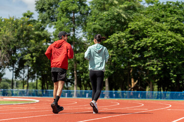Asian Couple jogging and running outdoors at sport stadium. Happy Man woman wearing sportswear...