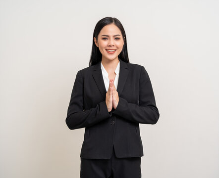 Happy young asian businesswoman doing sawadee gesture smiling to camera. Welcome greeting female in black suit. Attractive latin woman worker employee.