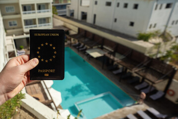 Man holding EU passport against the backdrop of a luxury hotel.