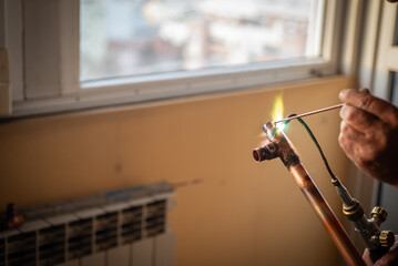 A worker welds copper pipes with a gas torch for central heating - obrazy, fototapety, plakaty