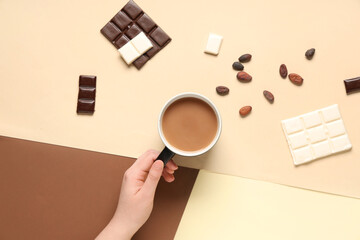 Female hand with cup of tasty hot chocolate and cocoa beans on color background