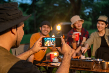 Group of asian people friend party camping in nature making toasting and taking photo by smartphone to share on social media. Hangout party outdoor in campsite nature on holiday weekend vacation