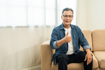 Handsome asian mature old man sitting on sofa couch in living room at home. Happy Portrait of...