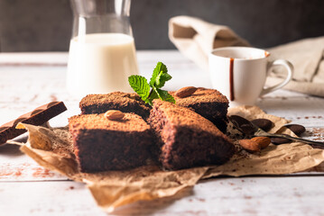 Many pieces of fresh chocolate brownie sprinkled with cocoa on a  bakery paper with glass of milk on white table. Homemade delicious chocolate pie