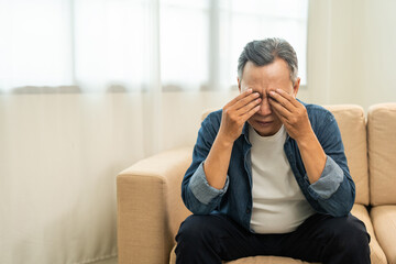 Asian mature old man sitting headache tired on sofa at home. Portrait of serious depression sadness...