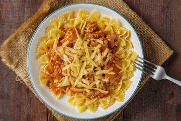 Bolognese pasta in a plate on a linen napkin next to a fork on a wooden table