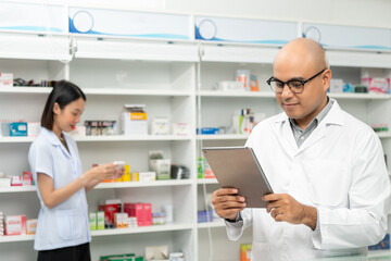Fototapeta premium Professional asian man pharmacist checks inventory arrangement of medicine in pharmacy drugstore. Male Pharmacist wearing uniform standing near drugs shelves counter prescription to customers